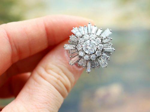 fig 2. A vintage 18ct white gold cluster ring featuring a central round brilliant cut diamond surrounded by a halo of brilliant cut diamonds and an outer sunburst tier of tapered baguette diamonds.