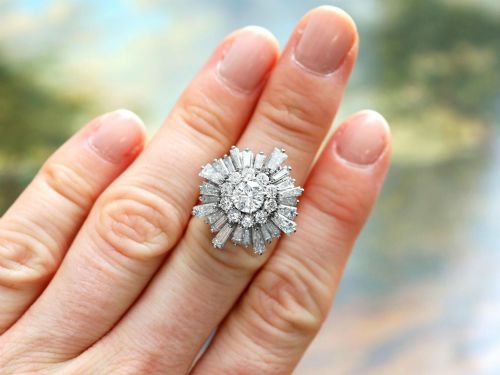 fig 3. A vintage 18ct white gold cluster ring featuring a central round brilliant cut diamond surrounded by a halo of brilliant cut diamonds and an outer sunburst tier of tapered baguette diamonds.