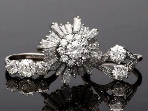 fig 5. A vintage 18ct white gold cluster ring featuring a central round brilliant cut diamond surrounded by a halo of brilliant cut diamonds and an outer sunburst tier of tapered baguette diamonds.