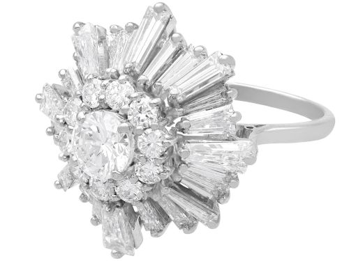 fig 7. A vintage 18ct white gold cluster ring featuring a central round brilliant cut diamond surrounded by a halo of brilliant cut diamonds and an outer sunburst tier of tapered baguette diamonds.