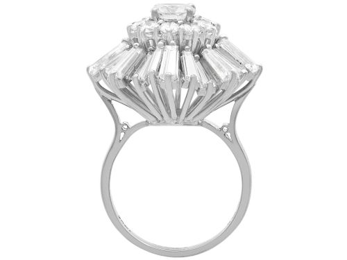 fig 9. A vintage 18ct white gold cluster ring featuring a central round brilliant cut diamond surrounded by a halo of brilliant cut diamonds and an outer sunburst tier of tapered baguette diamonds.