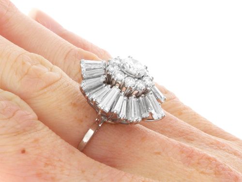fig 10. A vintage 18ct white gold cluster ring featuring a central round brilliant cut diamond surrounded by a halo of brilliant cut diamonds and an outer sunburst tier of tapered baguette diamonds.