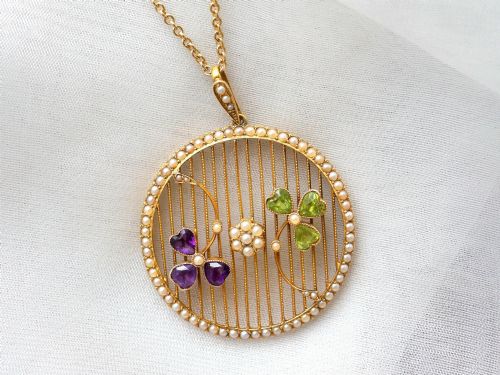 fig 6. A circular 18ct yellow gold openwork pendant set with seed pearls along the outer rim, containing peridot and amethyst trefoil motifs and a central seed pearl cluster.