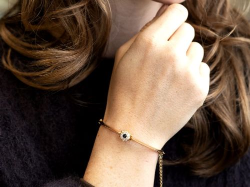 fig 3. An antique 15ct yellow gold hinged bangle featuring a central circular cluster of diamonds around a dark blue sapphire.