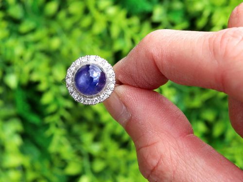fig 1. An Art Deco platinum cluster ring featuring a central cabochon star sapphire encircled by a halo of round diamonds with millegrain edging.