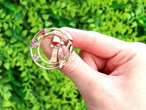 fig 1. A circular two-tone gold brooch featuring yellow gold concentric rings set with three pink spinels and decorated with a rose gold bow.