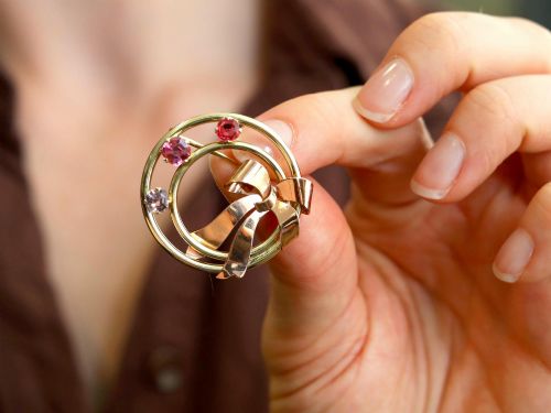 fig 2. A circular two-tone gold brooch featuring yellow gold concentric rings set with three pink spinels and decorated with a rose gold bow.