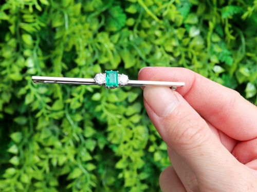 fig 1. An antique 18ct white gold bar brooch featuring a central rectangular emerald cut emerald flanked by two round diamonds on a slender horizontal metal bar.