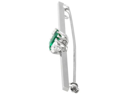 fig 6. An antique 18ct white gold bar brooch featuring a central rectangular emerald cut emerald flanked by two round diamonds on a slender horizontal metal bar.