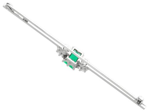fig 7. An antique 18ct white gold bar brooch featuring a central rectangular emerald cut emerald flanked by two round diamonds on a slender horizontal metal bar.