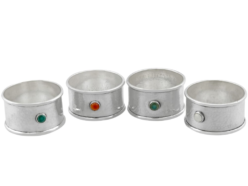 A set of four circular sterling silver napkin rings with planished hand-hammered textures, each inset with a distinct coloured cabochon stone.