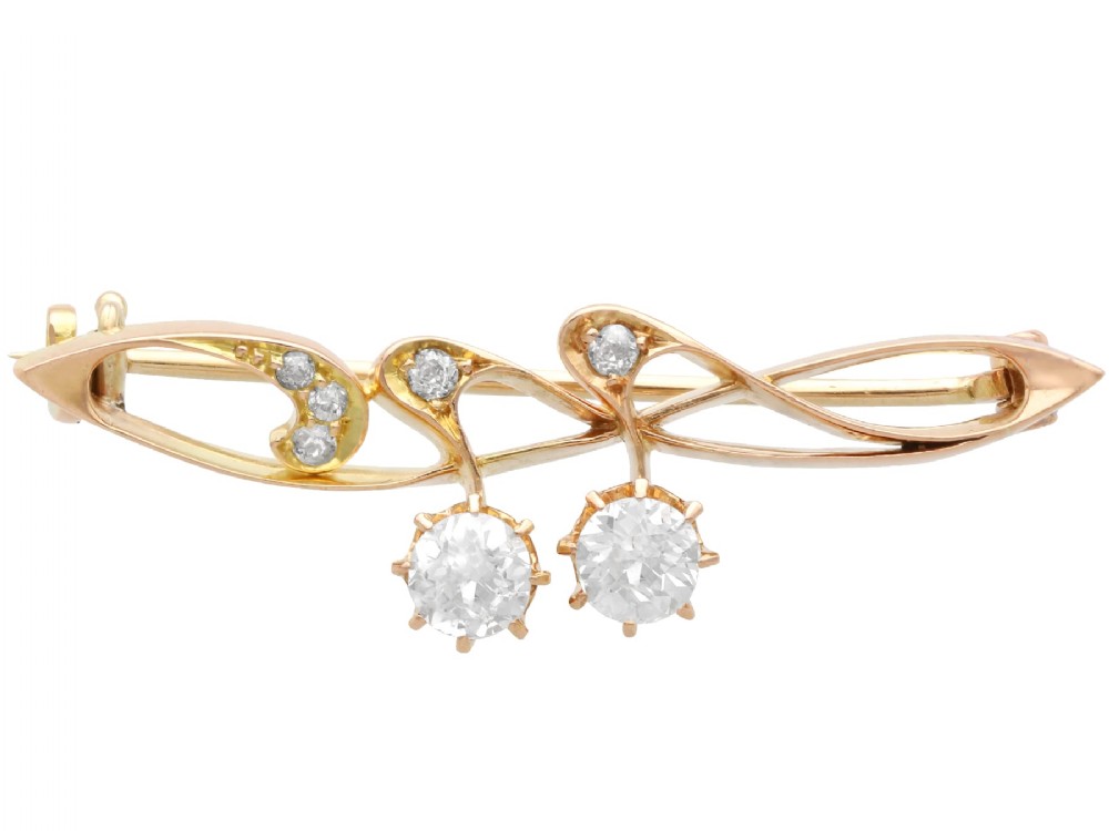 An antique 14ct yellow gold Art Nouveau bar brooch featuring openwork whiplash curves set with accent diamonds and two suspended claw-set diamonds.