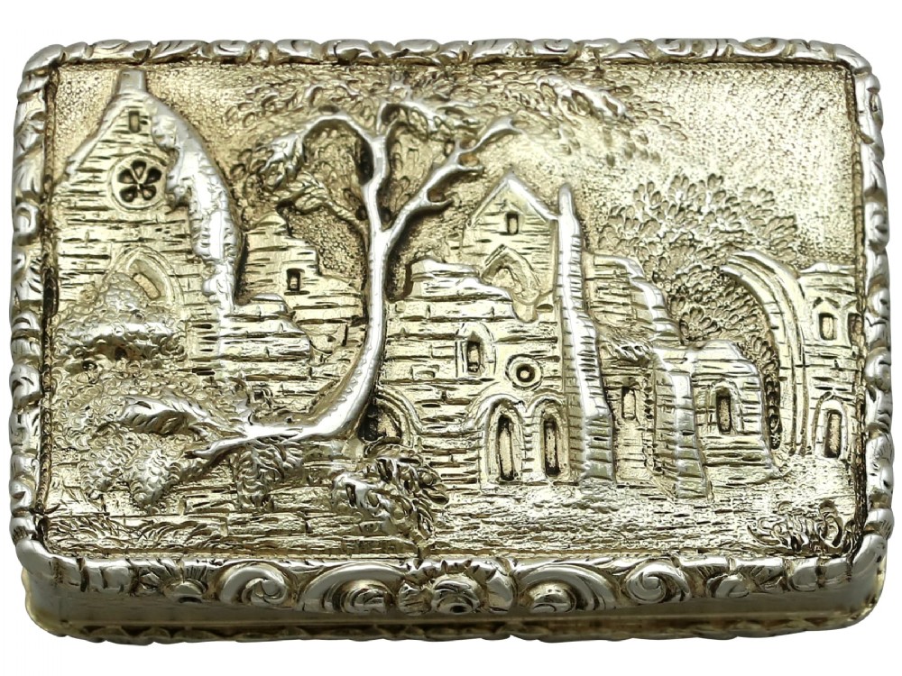 A rectangular sterling silver gilt vinaigrette featuring an embossed scene of architectural ruins surrounded by a scrolling border.