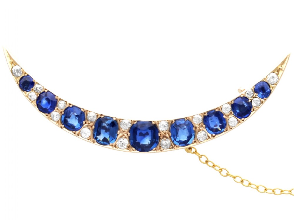 A crescent moon brooch set with graduated blue sapphires and accent diamonds in nine-carat yellow gold with an attached safety chain.