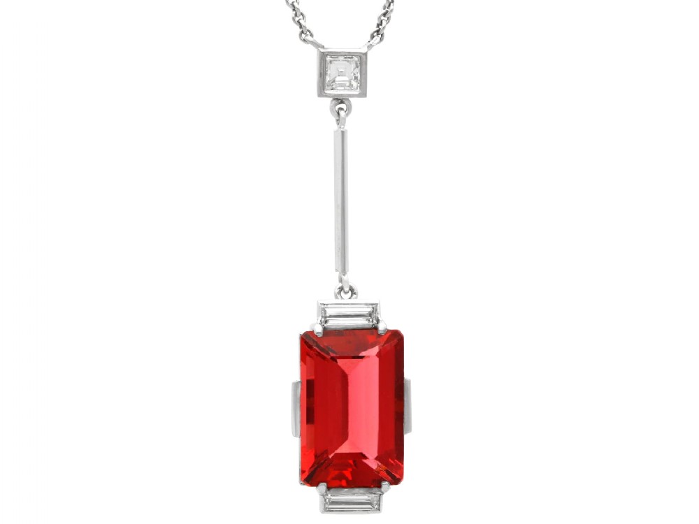 An Art Deco 18ct white gold pendant featuring a rectangular step-cut red tourmaline suspended from a bar link set with accent diamonds.