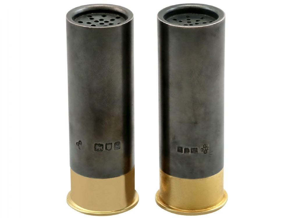 A pair of Edwardian sterling silver pepper shakers shaped like shotgun cartridges with dark silver bodies and gilt metal bases.
