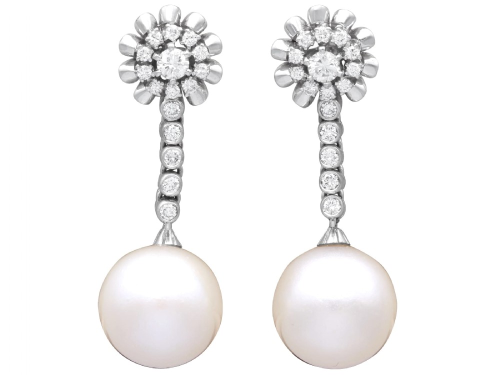 A pair of 18ct white gold drop earrings featuring round South Sea pearls suspended from articulated diamond stems and floral cluster stud tops.