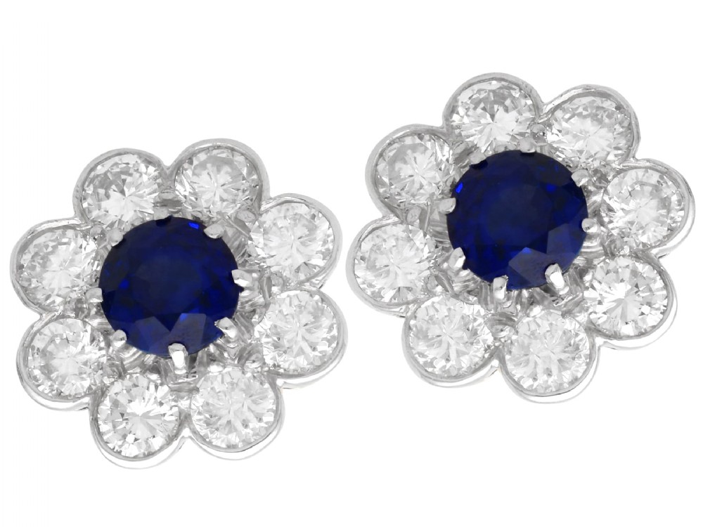 A pair of antique floral-shaped cluster earrings featuring central round blue sapphires encircled by bright diamonds.