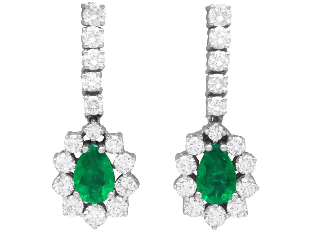 A pair of 18ct white gold drop earrings featuring pear-cut green emeralds surrounded by round diamond halos suspended from vertical diamond bars.