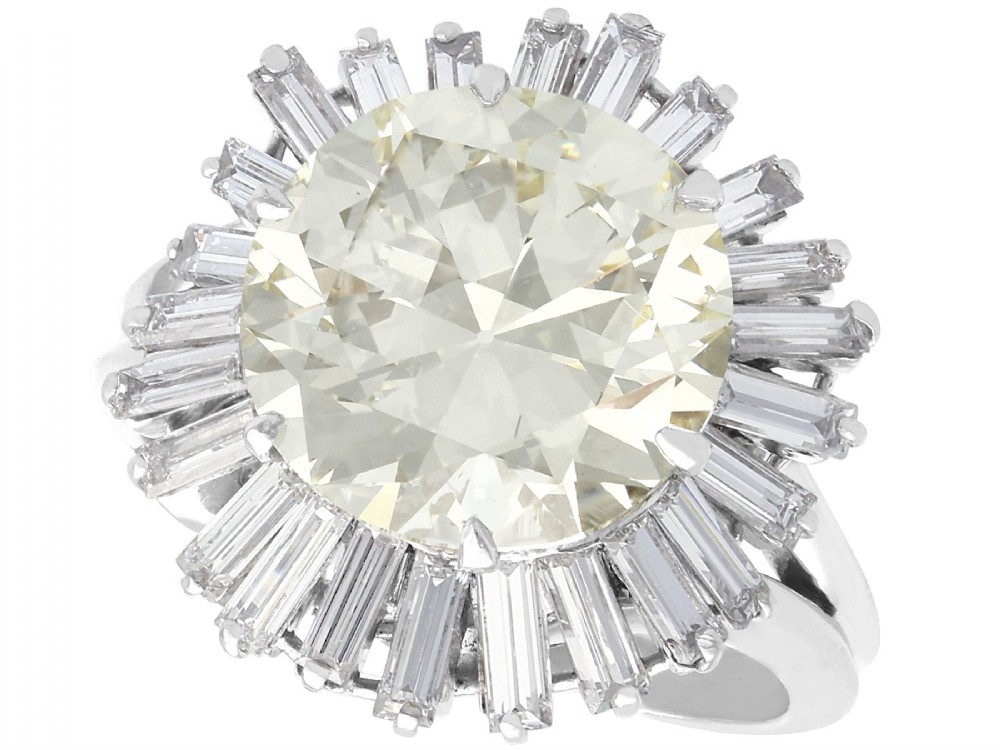 A platinum cocktail ring featuring a large round central diamond enclosed by a sunburst halo of baguette-cut diamonds.