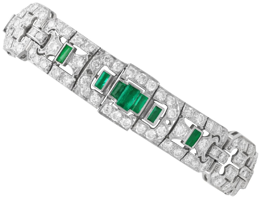 An Art Deco platinum strap bracelet featuring geometric links set with diamonds and green accent emeralds.