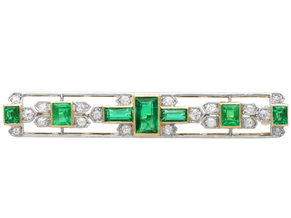 An elongated 9ct yellow gold bar brooch featuring a central step-cut emerald flanked by geometric diamond-set panels and smaller emerald accents.