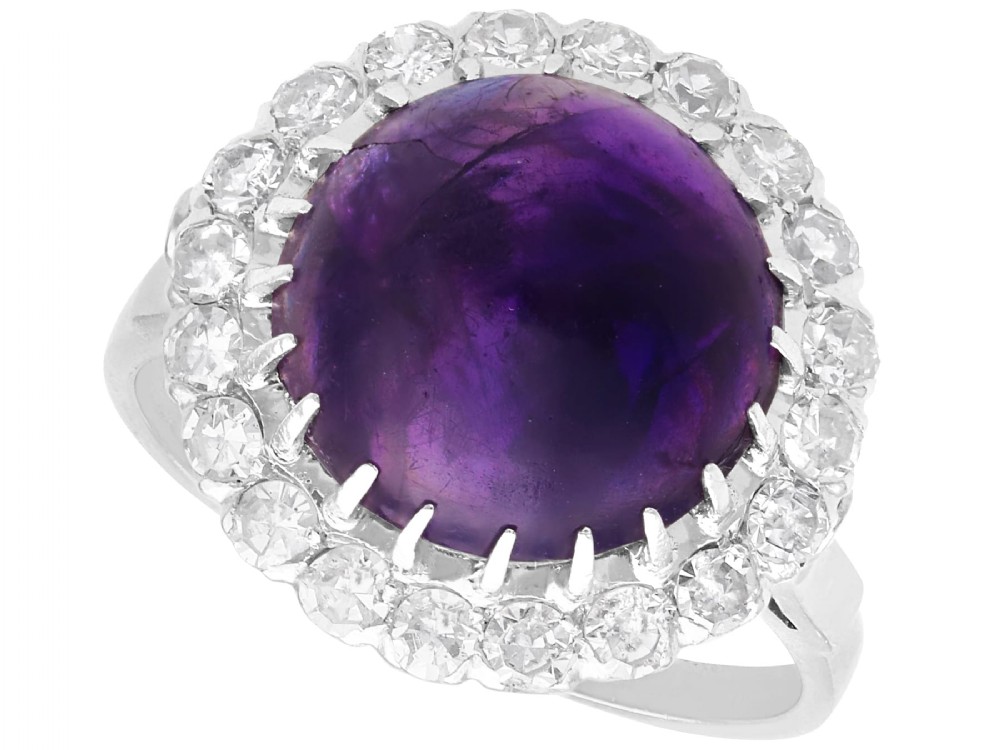 An antique platinum dress ring set with a large central purple cabochon amethyst surrounded by a halo of round diamonds.