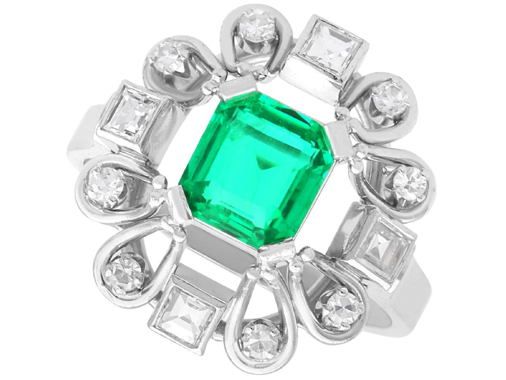 An Art Deco 18ct white gold ring featuring a central octagonal green emerald surrounded by geometric diamond-set loop mounts.