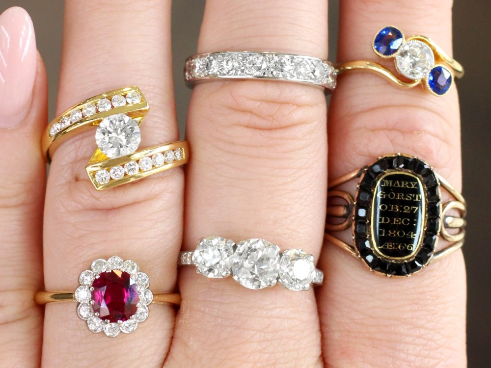 An 18ct yellow gold cluster ring featuring a central cushion cut red ruby framed by a halo of round diamonds. View IV