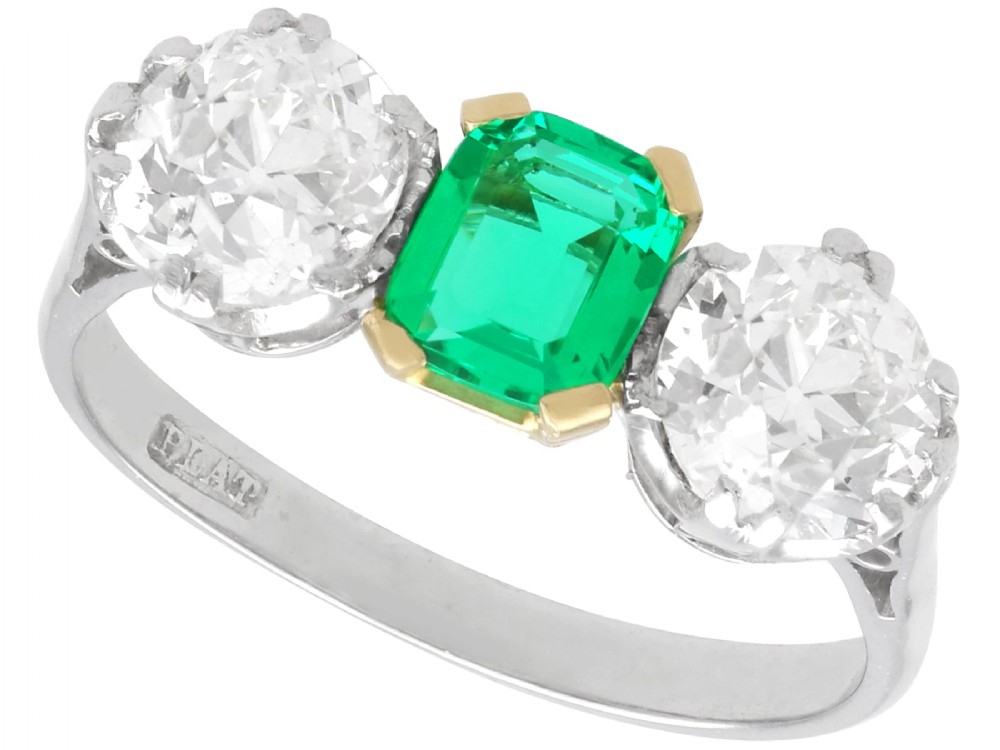 An Art Deco platinum trilogy ring featuring a central emerald-cut green emerald flanked by two round diamonds.