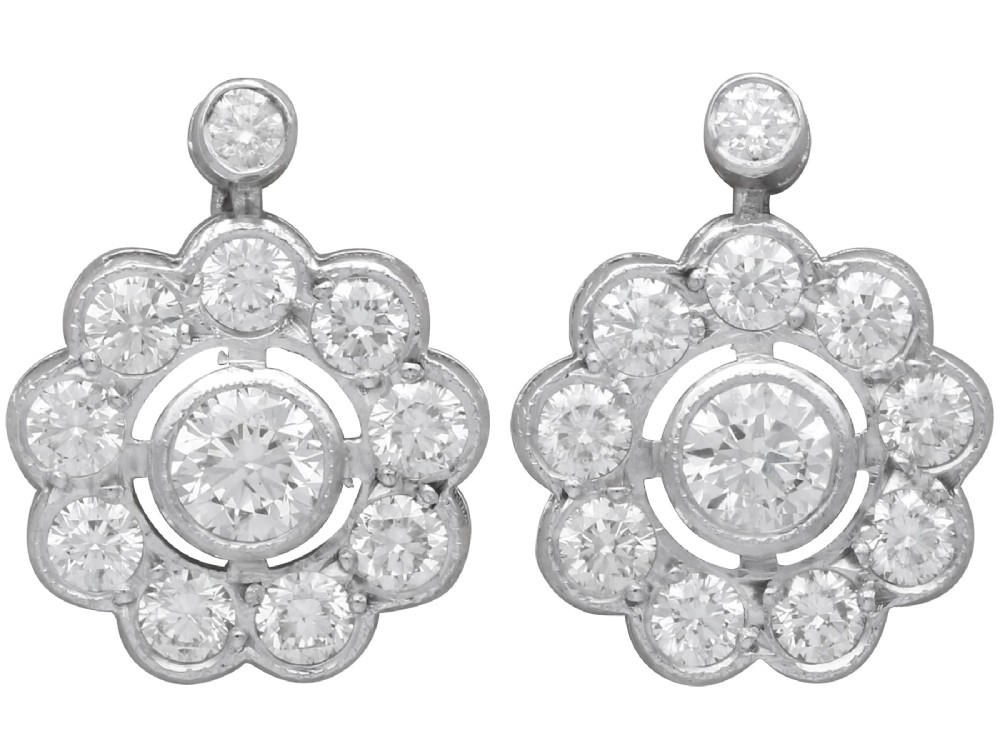 A pair of Art Deco 18ct white gold drop earrings featuring a circular diamond cluster motif suspended from a single bezel-set diamond surmount.