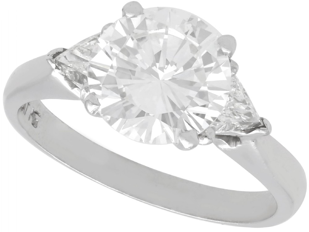 A vintage platinum ring featuring a large round brilliant central diamond flanked by two triangular side diamonds on a smooth metal band.