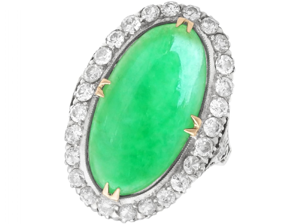 An antique Edwardian ring featuring a large oval green jadeite cabochon encircled by a halo of round diamonds on a gold band.