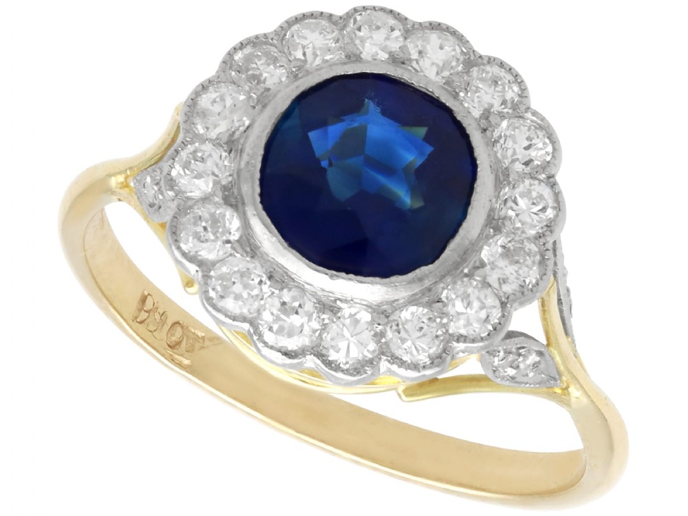 An antique 18ct yellow gold ring featuring a central round blue sapphire encircled by a halo of bright diamonds set within a scalloped millegrain bezel.