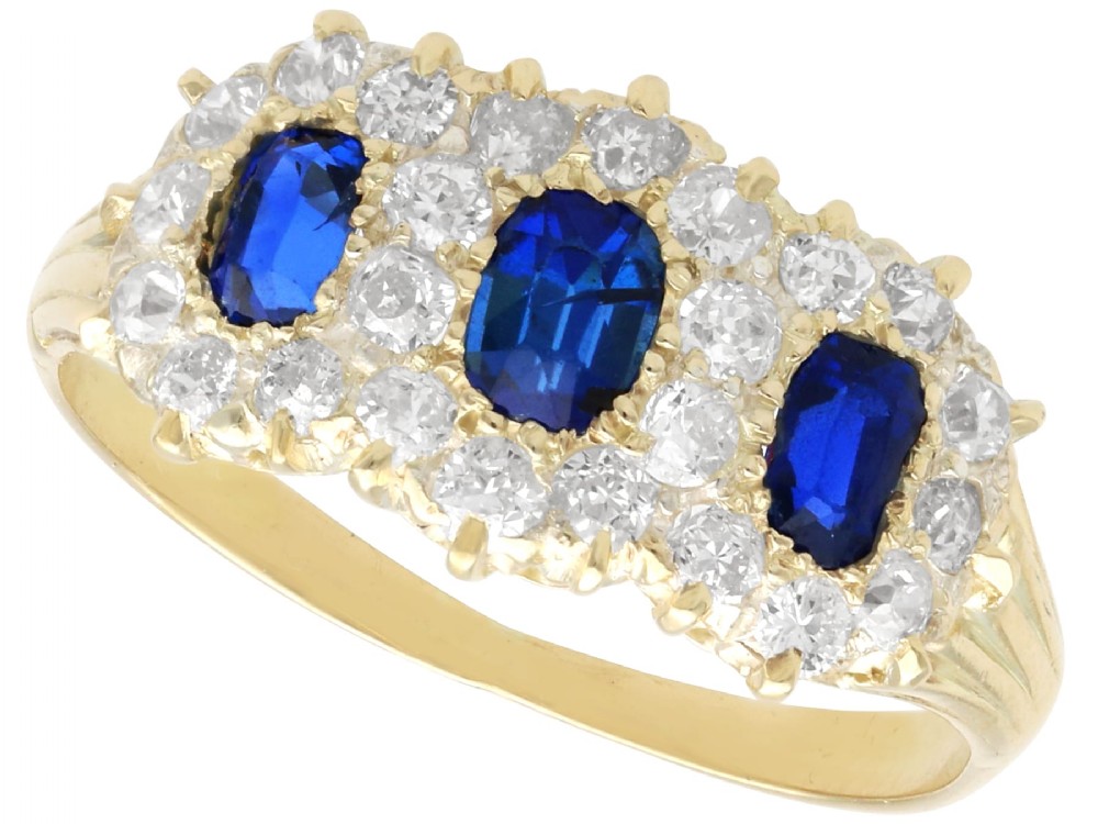 An antique 18ct yellow gold ring featuring three rectangular cushion-cut blue sapphires surrounded by a halo of old-cut diamonds.