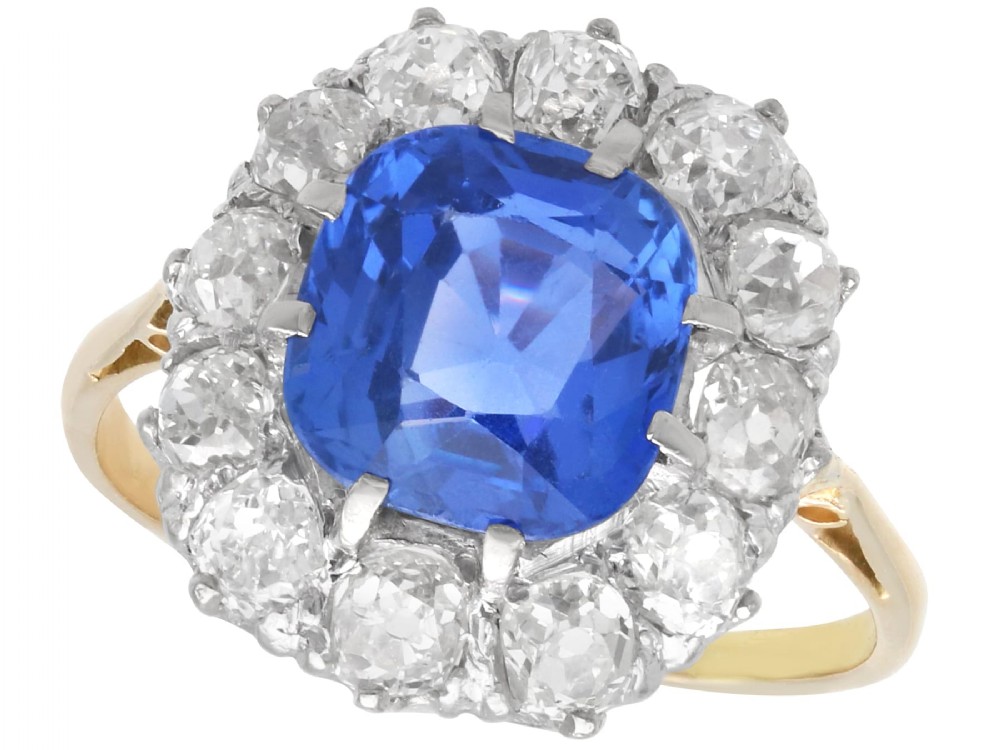 An antique Art Deco ring featuring a cushion-cut blue sapphire central stone surrounded by a cluster halo of round diamonds set on a yellow gold band.