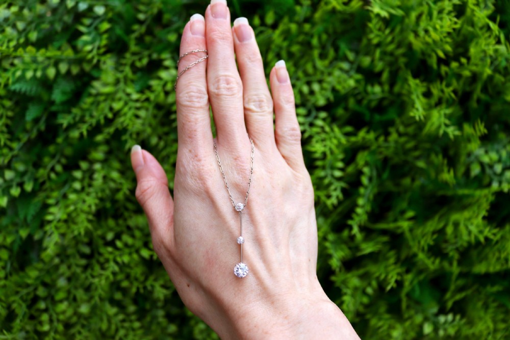 An 18ct white gold Art Deco pendant featuring three linear claw-set round diamonds suspended on a delicate chain. View II