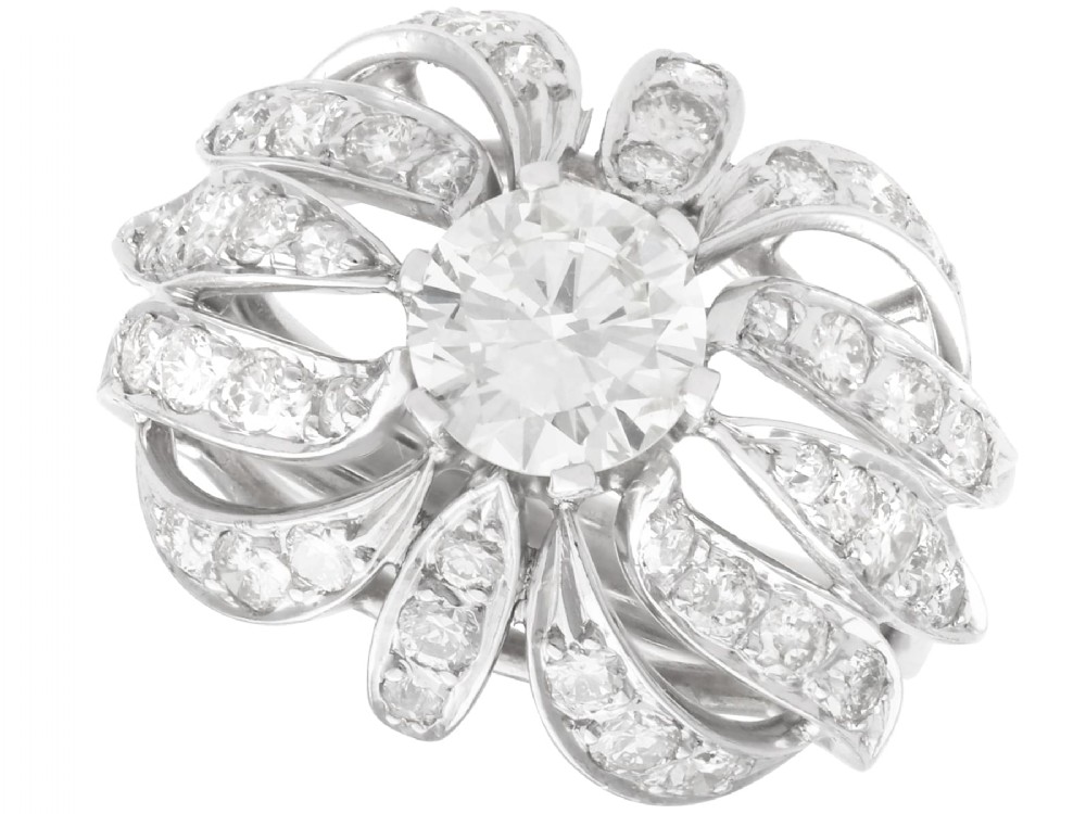 A platinum dress ring featuring a central round brilliant cut diamond surrounded by openwork diamond-set petal motifs.