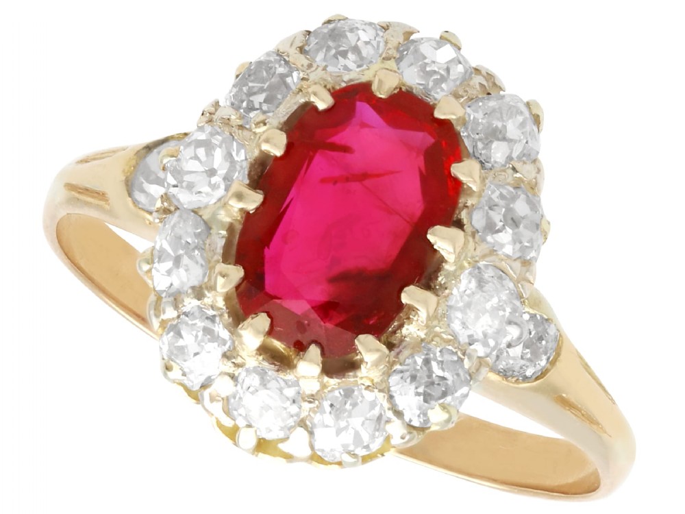 An 18ct yellow gold ring featuring a central oval faceted ruby surrounded by a halo of twelve old cut diamonds in claw settings.