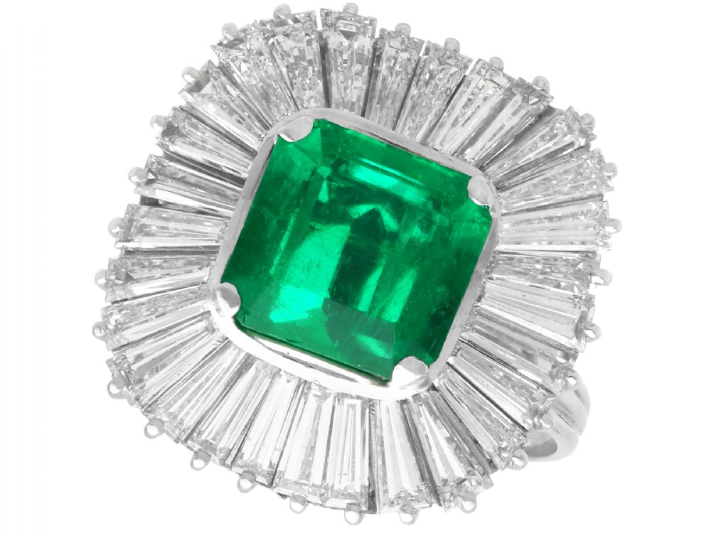 A 1950s platinum ballerina ring featuring a central rectangular emerald surrounded by a radiating fan of channel-set baguette cut diamonds.
