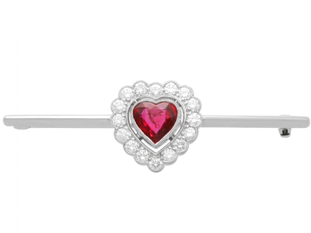 A vintage 18k white gold bar brooch featuring a central heart-cut red ruby framed by a diamond halo, mounted on a slender polished bar.