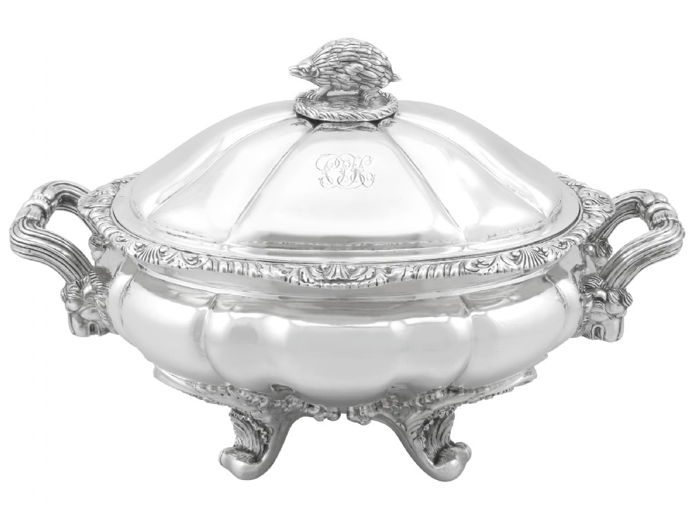 An antique silver soup tureen featuring a lobed body, scrolled acanthus feet, double side handles, and a domed lid topped with an animal finial.