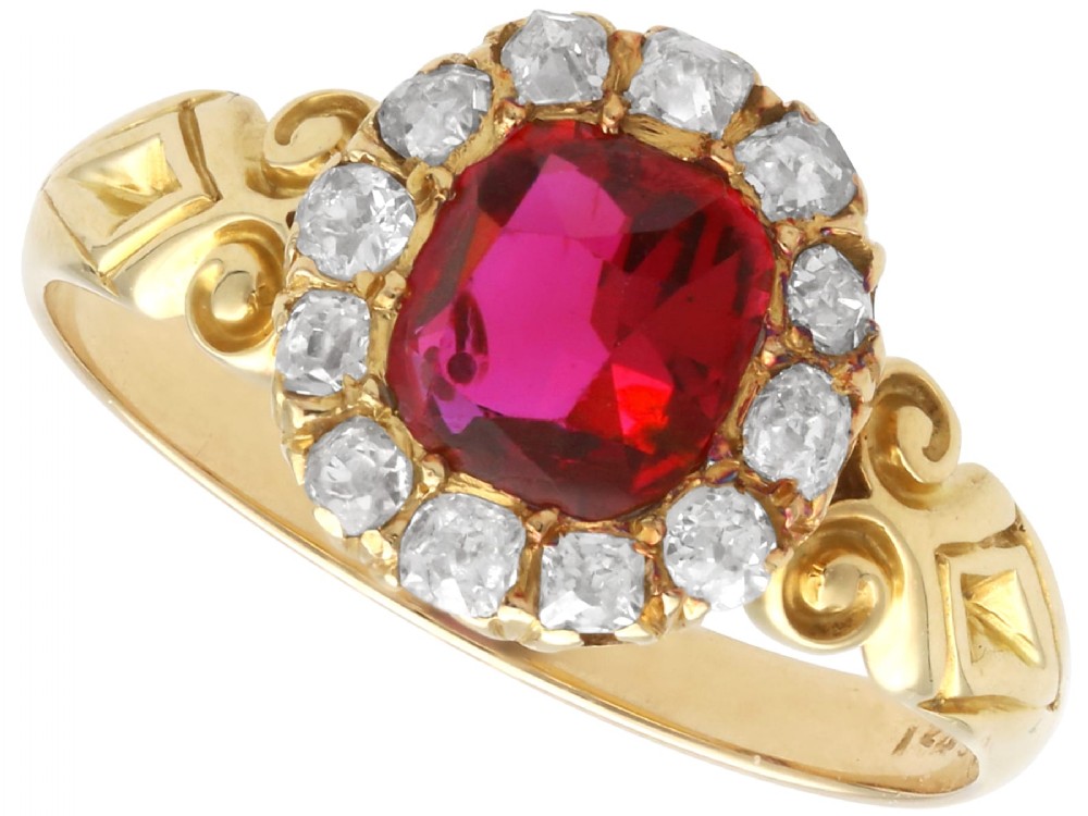 An 18ct yellow gold Victorian cluster ring featuring a central cushion-cut red ruby framed by twelve hand-cut diamonds with carved scroll shoulders.