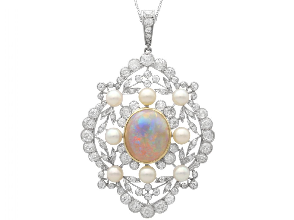 An antique platinum pendant featuring a central oval cabochon opal set in gold, surrounded by natural saltwater pearls and openwork diamond filigree.