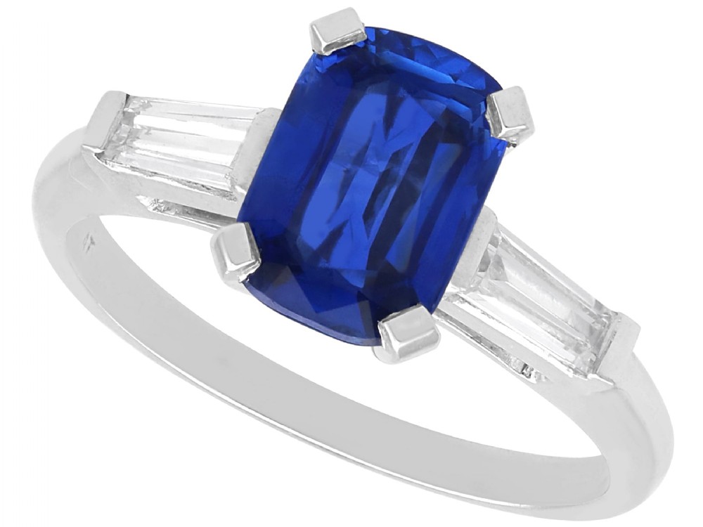 An Art Deco platinum ring featuring a central cushion-cut blue sapphire flanked by a stepped baguette-cut diamond on each shoulder.