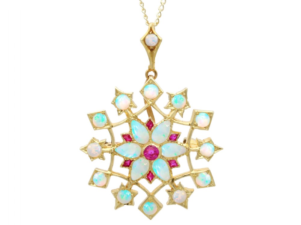 An antique 15ct yellow gold starburst pendant brooch set with cabochon opals and faceted rubies suspended on a gold chain.