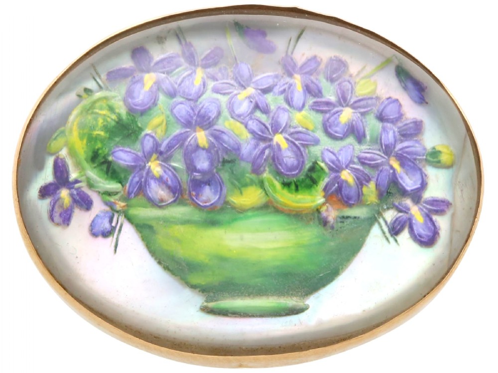 An oval 14ct yellow gold brooch set with a reverse-carved glass cabochon displaying purple violets in a green vase.