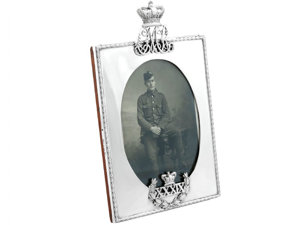 A rectangular sterling silver picture frame featuring an oval aperture, topped with a royal crown monogram and detailed with a laurel wreath emblem at the base.