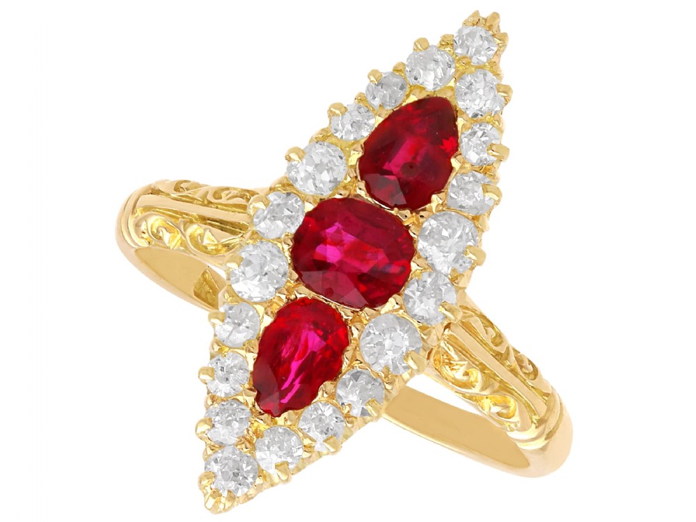 An antique 18ct yellow gold navette dress ring featuring three central red rubies surrounded by a border of diamonds and finished with scroll-carved shoulders.