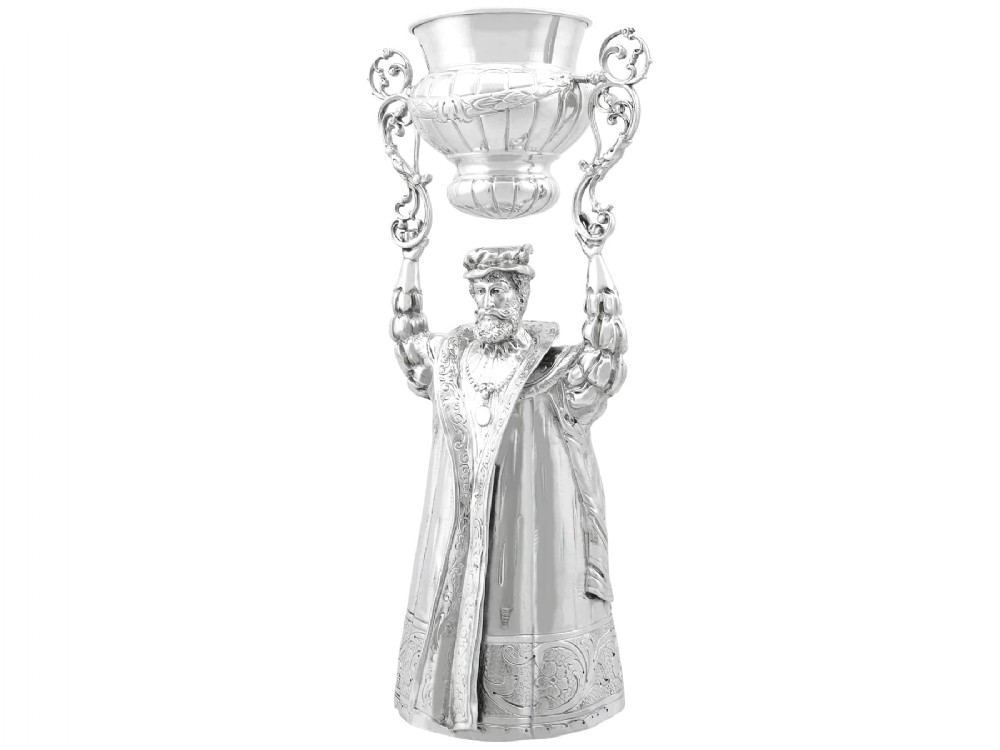 A Victorian sterling silver wager cup depicting a bearded male figure holding a double-handled vessel above his head.